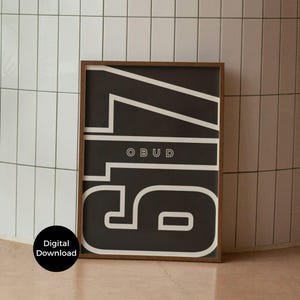 Könnte beinhalten: Ein gerahmter Kunstdruck mit einem auffälligen schwarz-weißen Grafikdesign. Das Kunstwerk zeigt die Zahl "15" in einer großen, stilisierten Schriftart, mit dem Wort "OBUD" darüber. Der Druck ist in einem dunkelbraunen Holzrahmen gefasst.