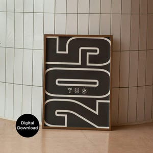 May include: A framed art print featuring the numbers and letters "205 TUS" in white against a black background. The print is encased in a brown wooden frame. A black circle with "Digital Download" is in the lower left.