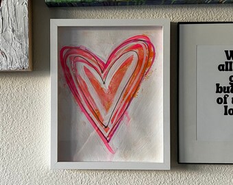 May include: A white framed painting of a pink and orange heart with black outlines on a white background.
