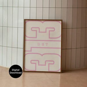 Może przedstawiać: Oprawiony wydruk artystyczny z napisem "DET" w jasnoróżowym, stylizowanym kroju pisma. Grafika umieszczona jest na kremowym tle i oprawiona w brązową drewnianą ramę. Czarno-biała naklejka "Digital Download" znajduje się w lewym dolnym rogu.