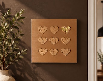 May include: A square canvas wall art piece featuring a grid of nine textured heart shapes in shades of brown, with one heart accented by gold leaf. The hearts are created with thick, raised paint strokes on a solid, smooth brown background.