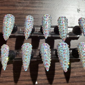 Puede incluir: Diez uñas postizas de stiletto azul claro con pedrería iridiscente.