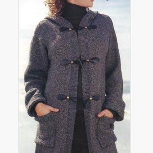 May include: A gray hooded toggle coat with large pockets. The coat has dark brown toggles and is worn by a person. The coat is made of a textured fabric. The person is wearing a black turtleneck. The background is a light blue and white.