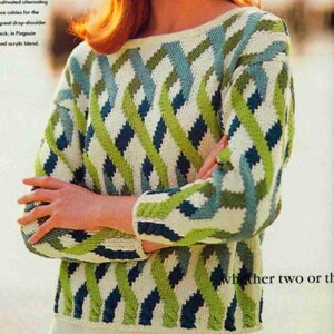 May include: A scoop-neck sweater with a geometric pattern in white, green, and blue. The sweater has long sleeves and a textured knit design. The model is wearing a blue headband.