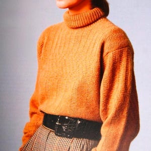 Pode incluir: Um suéter laranja de gola alta com textura canelada. O suéter é combinado com um cinto preto e uma saia xadrez. A modelo está usando o suéter e a saia em um fundo azul claro.