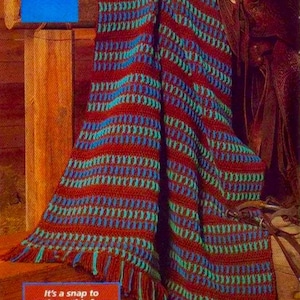 May include: A colorful afghan in shades of brown, aqua, and turquoise, with a fringed edge. The text "Old West" is at the top. The afghan is draped over a wooden surface.