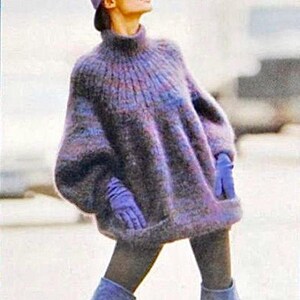 Könnte beinhalten: Ein übergroßer Strickpullover in Lila-, Blau- und Grautönen. Der Pullover hat einen hohen Rollkragen, lange Ärmel und eine lockere Passform. Passende lila Handschuhe und ein Hut vervollständigen den Look. Das Outfit wird mit dunkelgrauen Leggings und blauen Stiefeln kombiniert.