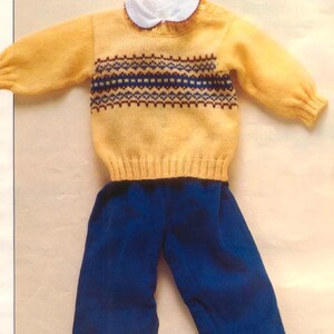 May include: A yellow knitted sweater and blue pants set for a baby. The sweater has a white collar and a patterned design in navy and brown. The text "18" and "Explained from 6-18 months" is in the top right corner. The outfit is paired with black shoes.