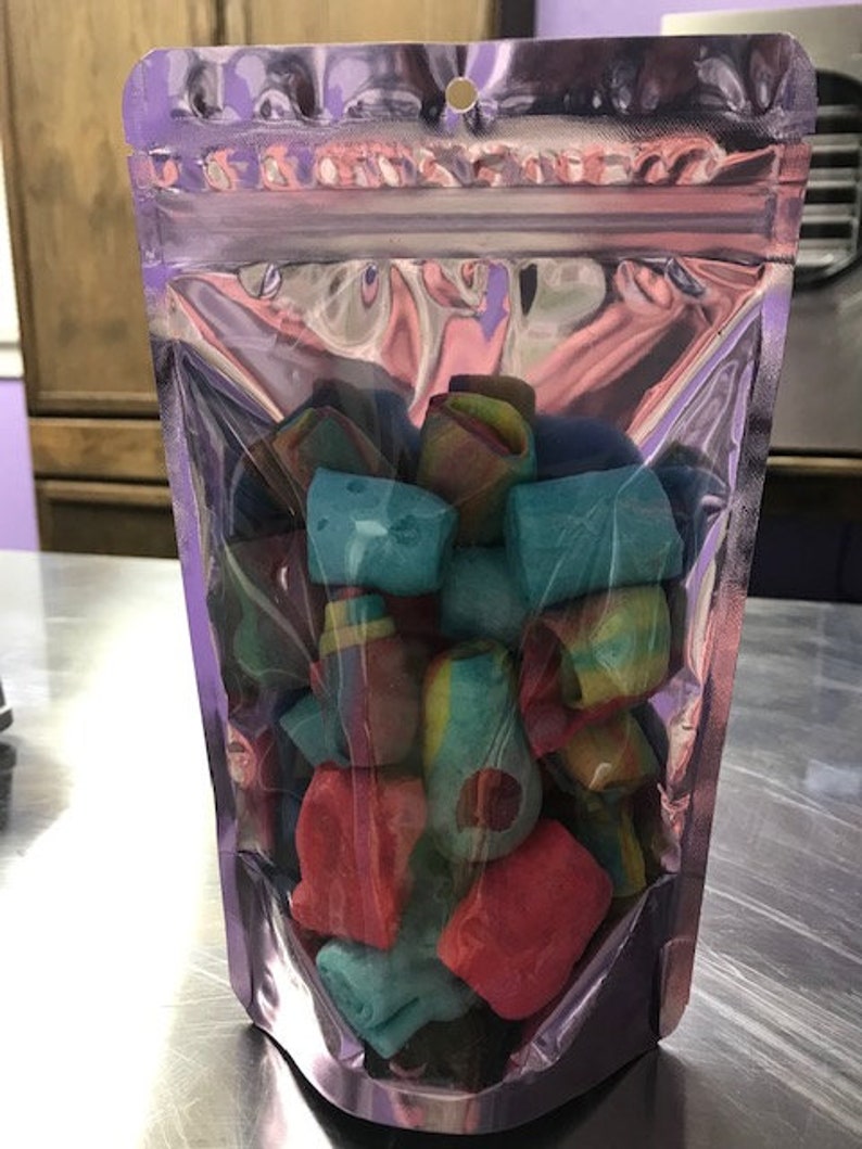 May include: A clear plastic resealable bag filled with colorful candy. The candy is in the shape of small, irregular blocks and is a mix of red, blue, green, and yellow.