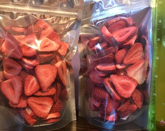 May include: Two clear plastic bags filled with dried strawberry slices. The bags are on a wooden surface with a ruler in the background.
