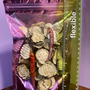 K&ouml;nnte beinhalten: Ein klarer, rosafarbener Plastikbeutel gef&uuml;llt mit getrockneten, geschnittenen Gurken und zwei roten Chilischoten. Ein flexibles Lineal liegt neben dem Beutel und zeigt cm-Messungen.