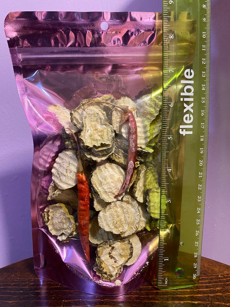 K&ouml;nnte beinhalten: Ein klarer, rosafarbener Plastikbeutel gef&uuml;llt mit getrockneten, geschnittenen Gurken und zwei roten Chilischoten. Ein flexibles Lineal liegt neben dem Beutel und zeigt cm-Messungen.