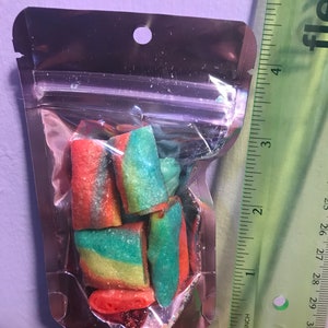 May include: A small clear plastic bag with a silver zipper closure contains a variety of colorful candy. The candy is in the shape of small, twisted tubes and is red, green, and yellow.
