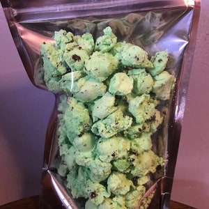 May include: A clear plastic bag filled with green and brown cookie dough bites. The bites are irregularly shaped and appear to be made with chocolate chips.
