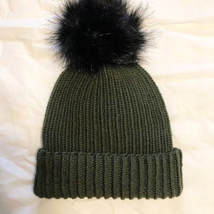 May include: A green knitted beanie with a black faux fur pom pom on top.