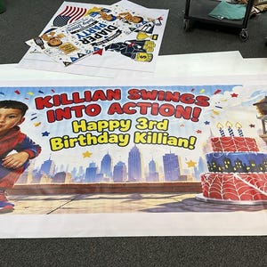 Puede incluir: Una pancarta de cumplea&ntilde;os rectangular de vinilo con un ni&ntilde;o en un disfraz de superh&eacute;roe rojo y azul. El texto dice "KILLIAN SWINGS INTO ACTION!" y "Happy 3rd Birthday Killian!" con un horizonte urbano, un pastel y regalos.