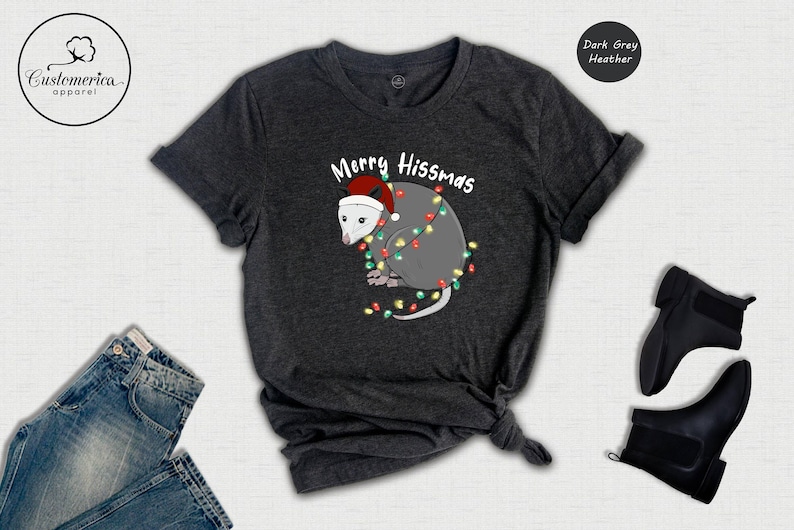 May include: A dark grey heather t-shirt with a white possum wearing a Santa hat and surrounded by Christmas lights. The text on the shirt reads 'Merry Hissmas'.