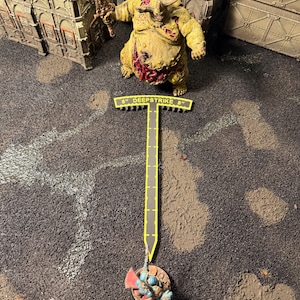 May include: A yellow T-shaped plastic measuring tool with the text 8" DEEPSTRIKE 8" printed in yellow on a black background. The tool is positioned between a large yellow monster miniature and a smaller blue armored miniature on a textured surface.