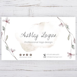 Op de afbeelding: Een witte visitekaartje met een aquarelontwerp van een tak met roze bloemen. De tekst op de kaart luidt "Ashley Logan, Professioneel logo ontwerp". De kaart bevat ook contactgegevens en social media-iconen.