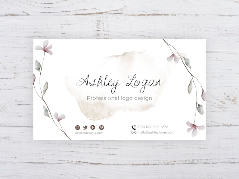 Op de afbeelding: Een witte visitekaartje met een aquarelontwerp van een tak met roze bloemen. De tekst op de kaart luidt "Ashley Logan, Professioneel logo ontwerp". De kaart bevat ook contactgegevens en social media-iconen.