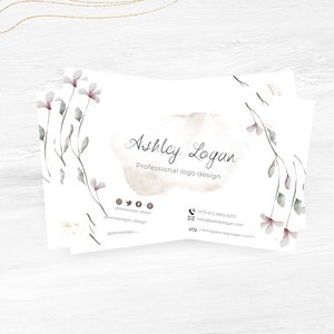 Op de afbeelding: Een witte visitekaartje met een aquarel bloemenontwerp en de tekst "Ashley Logan, Professioneel logo ontwerp". De kaart bevat ook contactgegevens, waaronder een telefoonnummer, e-mailadres en links naar sociale media.