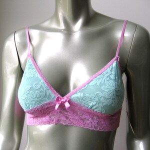 May include: A light blue and pink lace bralette with adjustable straps. The bralette has a delicate floral pattern and a bow detail in the center.
