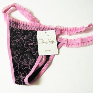 May include: Pink and black floral lace thong underwear with a pink ruffled trim. The underwear has a tag that reads "Rene Rofe Lingerie" and "S/Small".