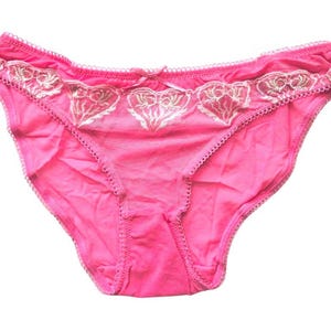 Puede incluir: Bragas rosas con delicado encaje blanco y un diseño de corazón.