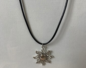 May include: A silver sun pendant necklace on a black cord.