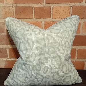 May include: A square cushion featuring a light grey leopard print design. The cushion has a textured surface and a neutral colour scheme, making it suitable for different interior styles. The cushion is designed for decorative purposes.