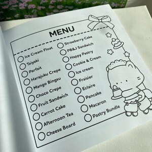 K&ouml;nnte beinhalten: Eine schwarz-wei&szlig;e Men&uuml;seite mit einer Liste von Desserts, darunter Eis, Cr&ecirc;pes und Kuchen. Das Wort "MENU" steht oben. Auf der rechten Seite der Seite befindet sich eine Cartoonfigur.