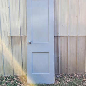 May include: A light blue, single-panel interior door with a raised panel design. The door has a simple knob and is leaning against a wall.