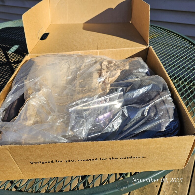 May include: A cardboard box containing a product wrapped in clear plastic. The box has the text "Designed for you, created for the outdoors." printed on the side. The date "November 03, 2025" is also visible.