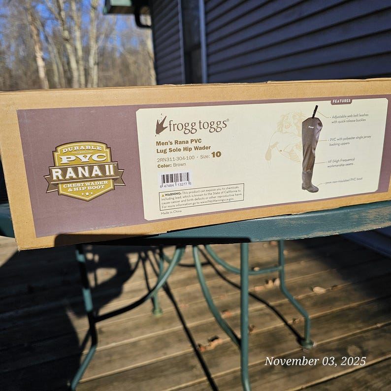 May include: A brown cardboard box featuring a pair of brown hip waders. The box has the text "frogg toggs" and "Men's Rana PVC Lug Sole Hip Wader." The size is 10. The box also has the text "DURABLE PVC RANAII CHESTWADER & HIP BOOT."