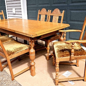 May include: A light brown wooden dining table with six matching chairs. The table has a rectangular top and ornate legs. The chairs have carved backs and upholstered seats. The set is made of wood and has a vintage style.