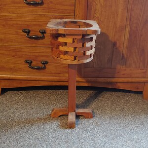 May include: A wooden plant stand with a square base and a single, tall, cylindrical post. The planter is made of stacked wooden pieces and has a natural wood finish.