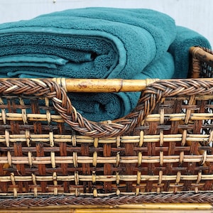 May include: A woven wicker basket with a brown and tan pattern, filled with folded teal towels.