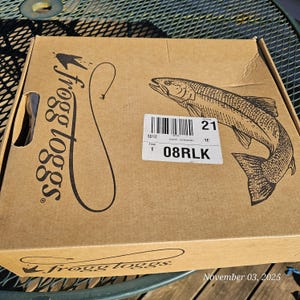 May include: A brown cardboard box with the "frogg toggs" logo and a fish illustration. The box has a shipping label with a barcode and the text "08RLK". The date "November 03, 2025" is visible.