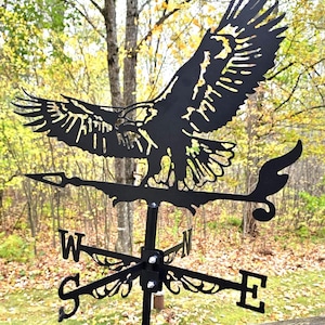 May include: Black metal weathervane featuring a soaring eagle with outstretched wings. The weathervane includes directional indicators: North, South, East, and West. The eagle is perched above the directional arms, adding a decorative touch to any outdoor space.