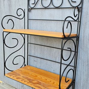 May include: Black metal wall shelf with two wooden shelves and decorative scrollwork.