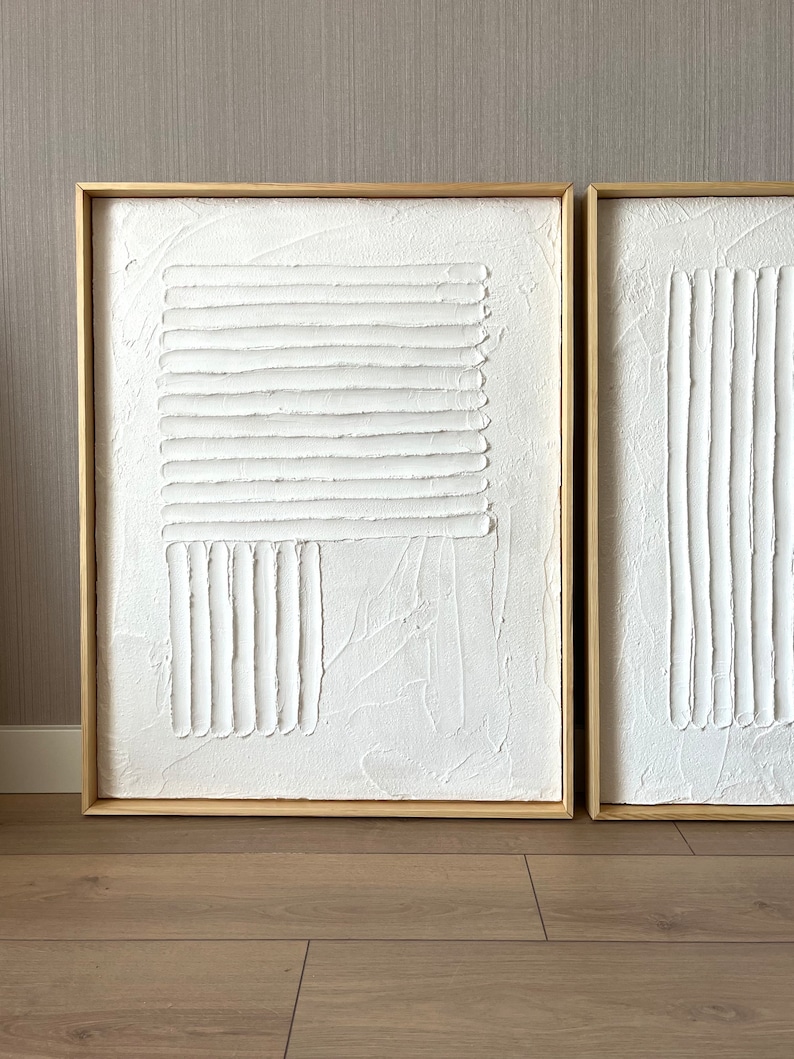 Puede incluir: Dos pinturas abstractas blancas texturizadas en marcos de madera. Las pinturas presentan l&iacute;neas en relieve y formas geom&eacute;tricas.