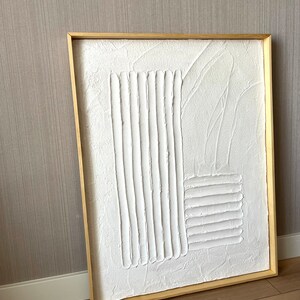 Puede incluir: Un lienzo blanco enmarcado con un dise&ntilde;o abstracto texturizado. El dise&ntilde;o est&aacute; formado por l&iacute;neas y formas en relieve, creando un efecto tridimensional.