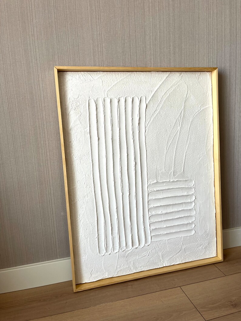 Puede incluir: Un lienzo blanco enmarcado con un dise&ntilde;o abstracto texturizado. El dise&ntilde;o est&aacute; formado por l&iacute;neas y formas en relieve, creando un efecto tridimensional.