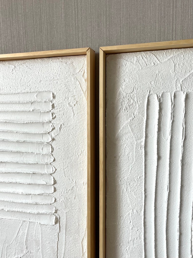 Puede incluir: Dos lienzos blancos texturizados con l&iacute;neas en relieve en un estilo abstracto moderno, enmarcados en madera natural.