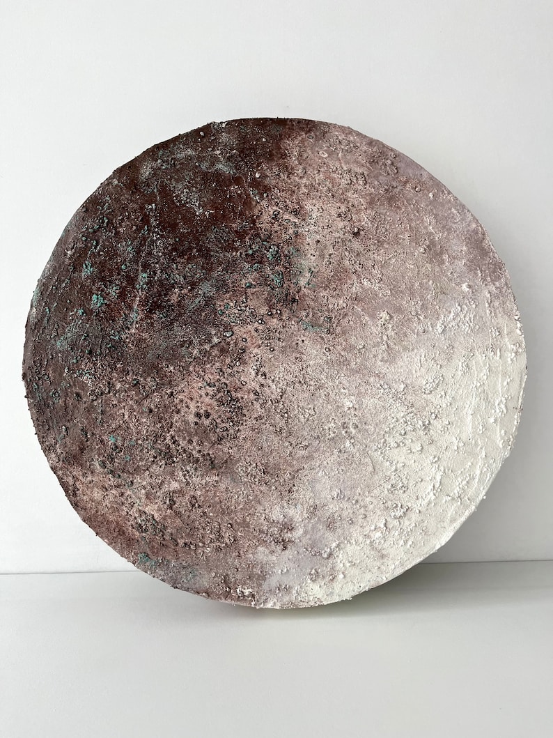 May include: A round, white and brown ceramic wall art piece with a textured surface. The piece has a gradient of color from dark brown to white.
