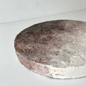 May include: A round, white and brown textured cake stand with a rough, uneven surface.