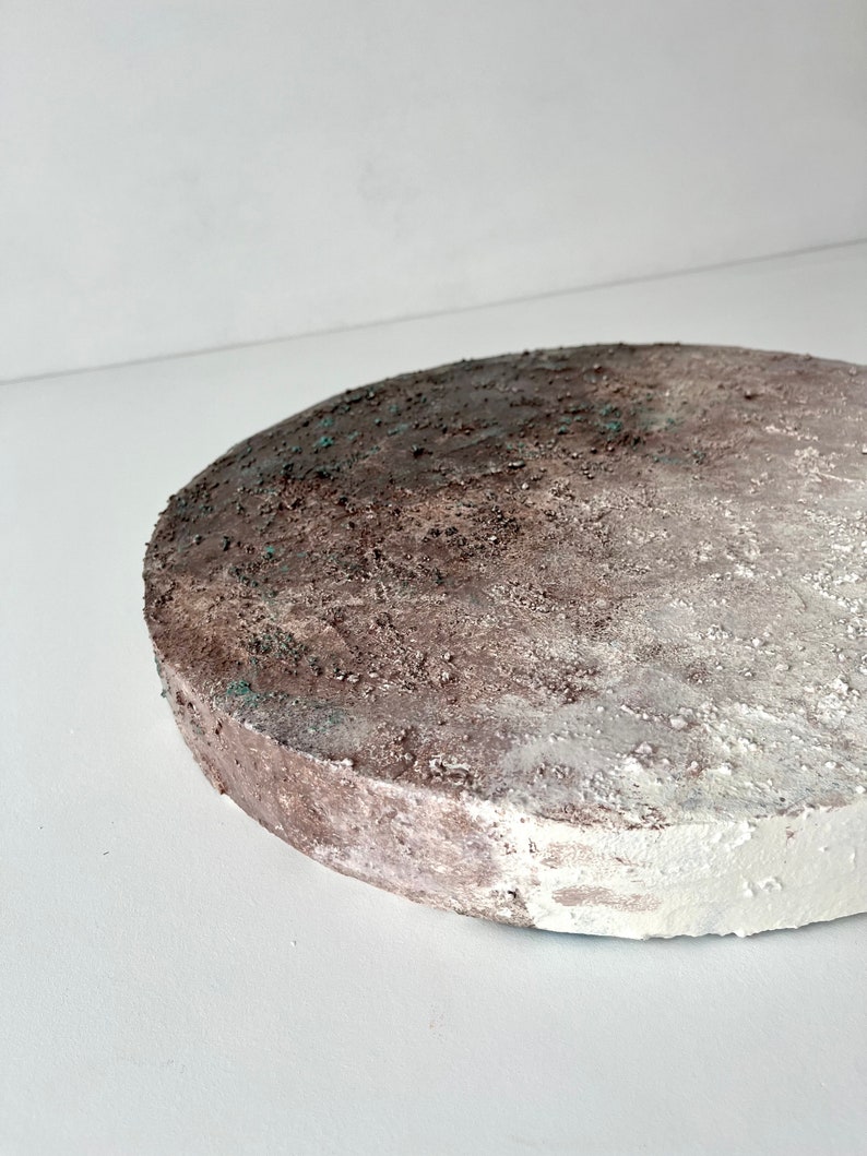 May include: A round, white and brown textured cake stand with a rough, uneven surface.