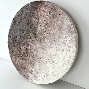 May include: A round, white and brown textured wall art piece with a subtle gradient effect. The piece has a rough, organic texture.