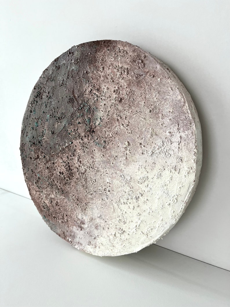 May include: A round, white and brown textured wall art piece with a subtle gradient effect. The piece has a rough, organic texture.