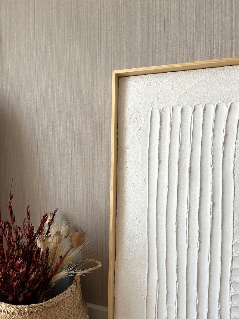 Puede incluir: Una pintura de lienzo blanco texturizado con un marco de madera. La pintura presenta una serie de l&iacute;neas verticales creadas con pintura blanca espesa.